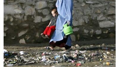 A woman swings her child over a drain as she carries a gas fuel canister, in Kabul, Afghanistan, the country with the world's worst record for maternal health.