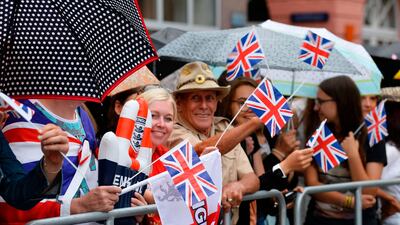Spectators wave with British flags and hide from rain under umbrellas as they wait for the visit of Britain's Prince William, Duke of Cambridge, and his wife Kate, the Duchess of Cambridge. AFP