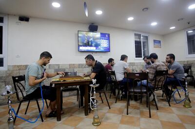 Palestinians play a board game and cards as television screen displays news about the results of Israel's parliamentary election, in a coffee shop in Hebron in the Israeli-occupied West Bank. Reuters