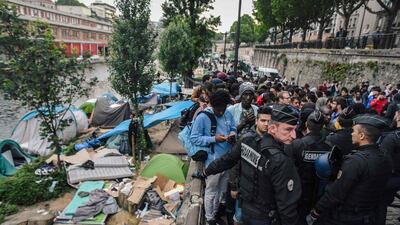French CRS anti-riot police officers stand guard by migrants and refugees queing during the evacuation by police of their makeshift camp along the Canal de Saint-Martin at Quai de Valmy in Paris, on June 4, 2018. More than 500 migrants and refugees were evacuated on early Monday from a makeshift camp that had been set up for several weeks along the Canal. Lucas Barioulet / AFP