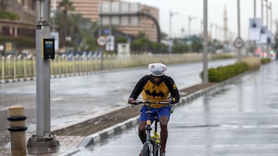 A cyclist rides with a bag on his head to stay dry as the rain comes down in Dubai. Chris Whiteoak / The National