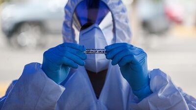 A healthcare worker holds a sample of a nasal swab after testing a passenger at a drive-thru new coronavirus testing site outside a supermarket in Santiago, Chile. AP Photo
