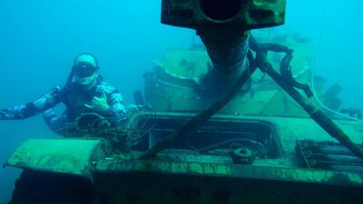 A diver poses next to the a sunk tank.