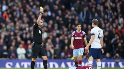 Referee Michael Oliver shows a yellow card to Oliver Skipp of Tottenham as Michail Antonio of West Ham United lies injured. Getty