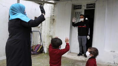 Islam Bseileh, a 29-year-old Palestinian who used to work in Israel, waves to his wife and two kids (all wearing masks) as he receives food they delivered to him while in quarantine in his home in the city of Hebron in the occupied West Bank. AFP