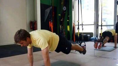 1. Position the TRX so that it is mid-calf length. Lay down on your front, keeping your feet in the foot cradles without touching. Hands should be shoulder-width apart, fully extended in the press-up position. Photos by Kumar Satish / The National