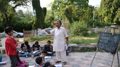 Muhammad Ayub,, an employee with Pakistan's Civil Defence service, teaches sum children at a makeshift school in a park in Islamabad. He charges nothing and many of his pupils have gone on to university and jobs in government and business. Aamir Qureshi / AFP HI