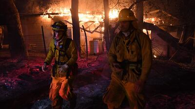 Firefighters move away from a burning house after discovering downed live power lines, as the Thomas wildfire continues to burn in Carpinteria, California. Mark Ralston / AFP