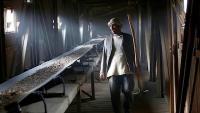 A worker observes a conveyer belt carrying broken rocks to be ground.