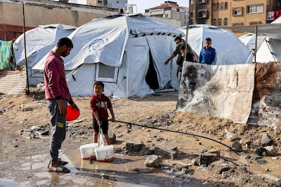 A boy filling up buckets with water from a hose near tents at a shelter in Gaza city on Wednesday. AFP