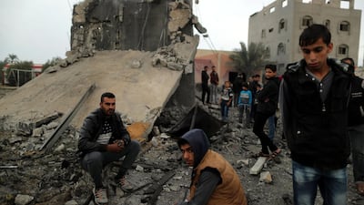 Palestinians sit at the remains of a building. Reuters