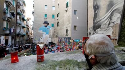 A man wearing a protective face mask stands in front of a mural depicting Diego Maradona, as people gather to mourn his death in Naples. Reuters