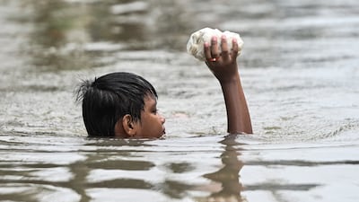 A boy holds uncooked spring rolls as he wades through a flooded area after a heavy overnight rain in Barangay Marulas, Kawit, Cavite. Reuters