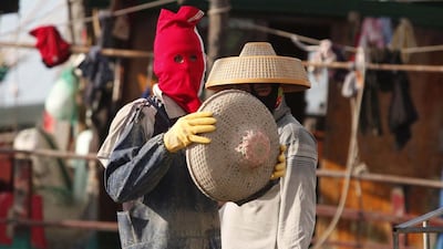 A man wearing a red face cover prepares to put on a hat as he repairs fishing nets at a port in Hainan. John Ruwitch / Reuters