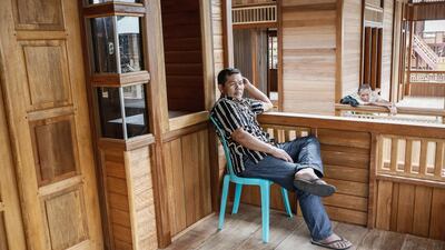 A constructor awaits customers on the porch of a newly built wooden house. Putu Sayoga / Getty Images