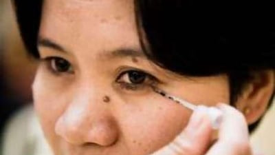 A customer applies newa kohl, an eyeliner made by Noura al Mazrouie from crushed date seeds, at the Liwa Date Festival. "Every bit of the date is beneficial," says Mrs Mazrouie.