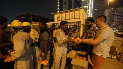 Volunteer Dan Cross, right, and Tahir Shah, second right, from Moti Roti give iftar food to labourers at a building site in the Tecom area of Dubai. Pawan Singh / The National
