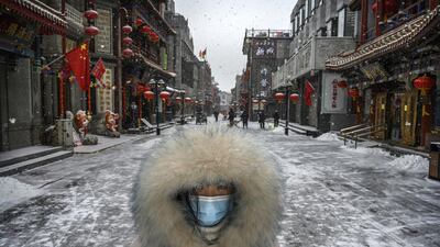 A Chinese woman wears a protective mask as she walks during a snowfall in an empty and shuttered commercial street in Beijing, China. Getty