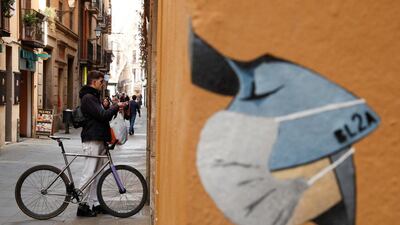 A man stops with a bicycle near a drawing of a person wearing a mask in a wall, in central Barcelona, Spain. Reuters
