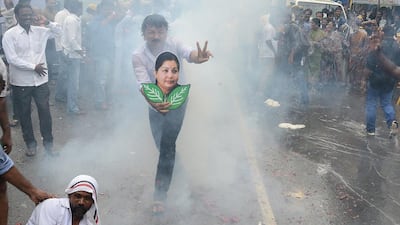 A worker from the All India Anna Dravida Munnetra Kazhagam party (AIADMK) flashes a victory sign and carries an image of AIADMK head, Jayalalithaa Jayaram, as supporters set off fireworks during celebrations of her successful bail application, in Chennai on October 17. AFP Photo