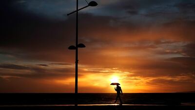 A man walks in the rain as the sun sets in Ayia Napa, Cyprus. Petros Karadjias / AP Photo
