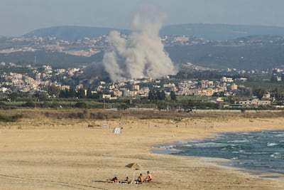 People sunbathing on Tyre Beach as smoke rises from the site of an Israeli air strike in the village of Deir Qanoun. AFP