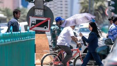 Pedestrians protect themselves from the sun with umbrellas while crossing a street at downtown Abu Dhabi. Victor Besa / The National