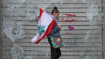 An anti-government protester walks with a Lebanese national flag past a broken window in downtown Beirut. AFP