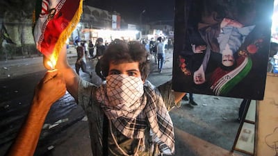 An Iraqi protester holds up an Iranian flag as another sets it on fire for him, next to a portrait depicting Iran's former and current Supreme Leaders. AFP