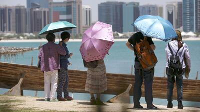 A group of Chinese tourists shield themselves from the midday sun as they visit the Breakwater Corniche in Abu Dhabi. Silvia Razgova / The National