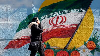 An Iranian woman speaks over phone while walking past a mural of the Iranian national flag in Tehran. EPA