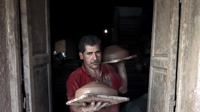 An Egyptian worker carries clay pots to be dried before displaying them for sale.