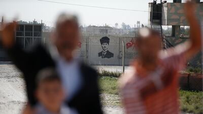 Backdropped by a graffiti depicting modern Turkey's founder Mustafa Kemal Ataturk, supporters of Turkey's Nationalist Movement Party (MHP) pose for photos at the border between Turkey and Syria, in Akcakale, Sanliurfa province, southeastern Turkey. AP Photo