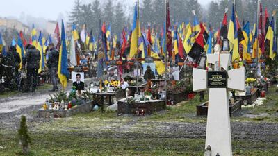 Ukrainian soldiers at Lychakiv cemetery in Lviv in May 2022, top, carry the coffin of a colleague killed during the Russian invasion. Below, the graves of Ukrainian soldiers at the cemetery on February 8, 2024. AFP