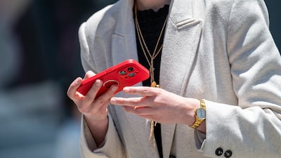 A pedestrian holds an iPhone in front of an Apple store in San Francisco, California, US, on Tuesday, June 11, 2024. Apple Inc. shares rose to a record after it took the wraps off long-awaited new artificial intelligence features, betting that a personalized and understated approach to the technology will win over customers. Photographer: David Paul Morris / Bloomberg