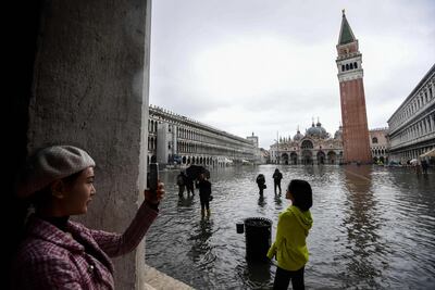 TOPSHOT - Tourists take photos on the flooded St. Mark's Square, by the Bell Tower (Rear R) and St. Mark's Basilica (Rear C) on November 24, 2019 in Venice during a high tide "Acqua Alta" meteorological phenomenon with a high of 140 cm expected. Flood-hit Venice was bracing for another, though smaller, high tide on November 24, after Italy declared on November 15 a state of emergency for the UNESCO city where perilous deluges have caused millions of euros worth of damage. / AFP / Miguel MEDINA