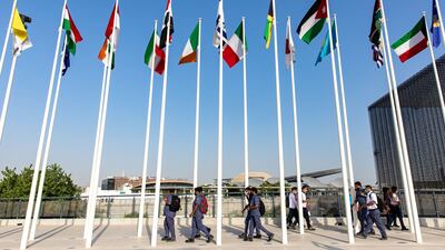 Men walk pass flags of the world's nations at the entrance to the Expo 2020 site in Dubai. Bloomberg