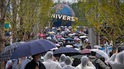 People wearing raincoats and carrying umbrellas walk through a plaza near the entrance of Universal Studios Beijing. AP Photo