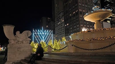 A woman sits on the steps of a fountain decorated for Christmas after the lighting of what's been described as "the world's largest Hanukkah menorah, in New York, on the first night of Hanukkah, the annual eight-day Jewish festival of lights. Due to coronavirus restrictions, a limited and socially-distanced crowd was allowed to attend. AP
