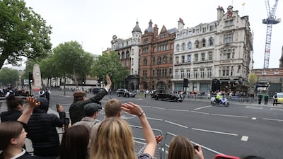 Members of the public wave at the Prince of Wales and the Duchess of Cornwall as they travel down Whitehall in central London. PA