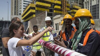 Dana El-Kalache and Ammar Al Alwan distribute water to workers on a construction site as part of the Sameness Project's campaign during the hot summer months. Antonie Robertson / The National