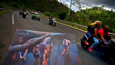 A printed photograph taken on September 28, 2017 shows people bathing on the highway after Hurricane Maria destroyed people's homes. Today motorcyclists ride by in Naranjito, Puerto Rico.