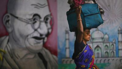 A migrant woman carries her belongings on her head as she walks past a painting of Mahatma Gandhi to board a train to her home state, at Hyderabad Railway Station in Hyderabad, India. AP Photo