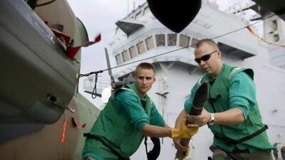 Two mechanics carry munitions to a combat helicopter, on the deck of the French navy vessel BPC Tonnerre in the Mediterranean sea.