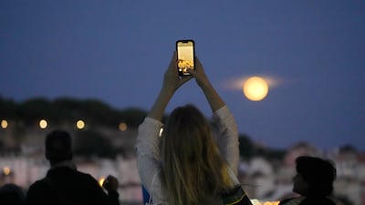 A woman takes pictures of a supermoon rising above Lisbon. AP
