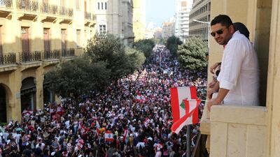 A man holds a Lebanese flag as he stands on a balcony during a protest targeting the government over an economic crisis, in Beirut, Lebanon. Reuters