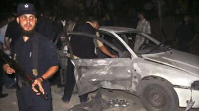 A Palestinian Hamas police officer stands guard as others inspect a damaged car following the explosion in Gaza City.