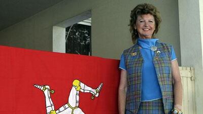 Gil Costain-Salway stands beside the Isle of Man flag at her residence in Dubai. The former airline worker runs quizzes every month for the Dubai Manx Society.