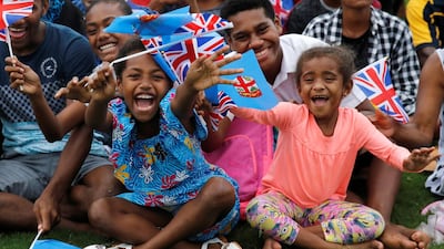 Children smile and wave British and Fijian flags. Reuters