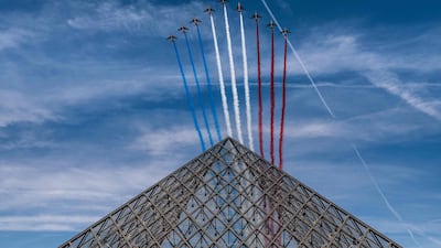 French elite acrobatic flying team "Patrouille de France" (PAF) release smoke in the colours of the French flag as they perform a fly-over the Louvre Pyramid during the Bastille Day military parade in Paris on July 14, 2022. (Photo by Martin BUREAU / AFP)